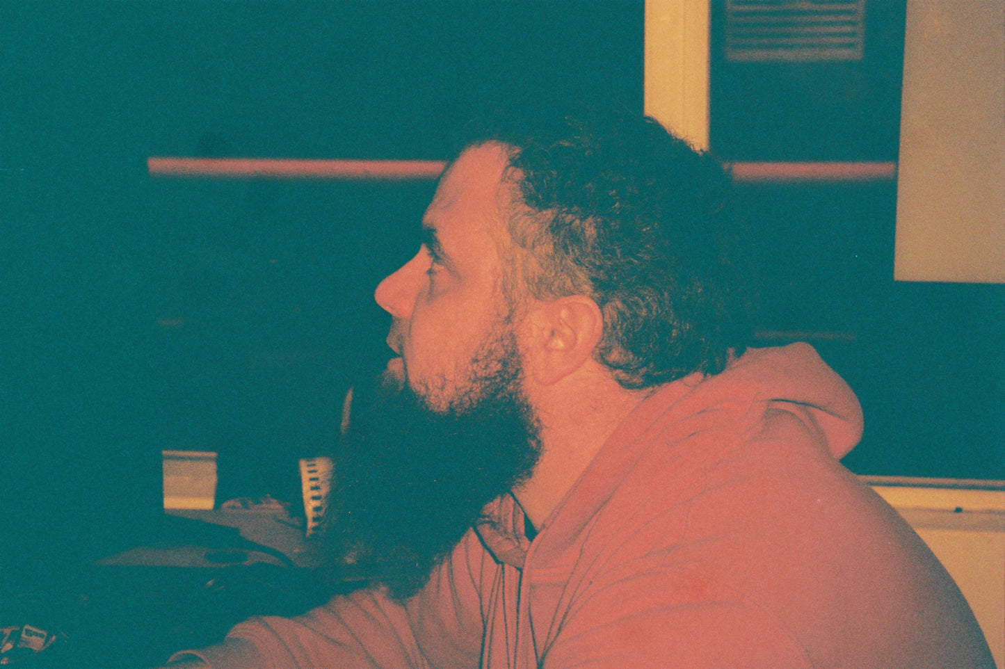 Redscale sample shot of a bearded man in a hoodie in profile indoors, teal and pink tones
