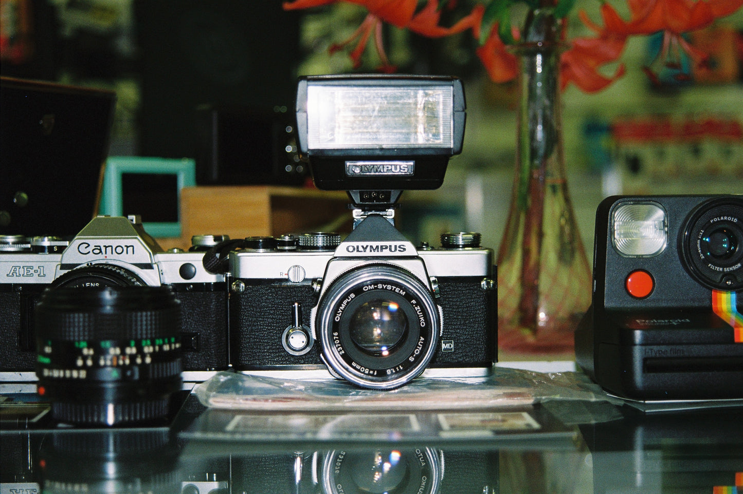 Vintage cameras including a Canon and Olympus on a reflective surface with a blurred background.