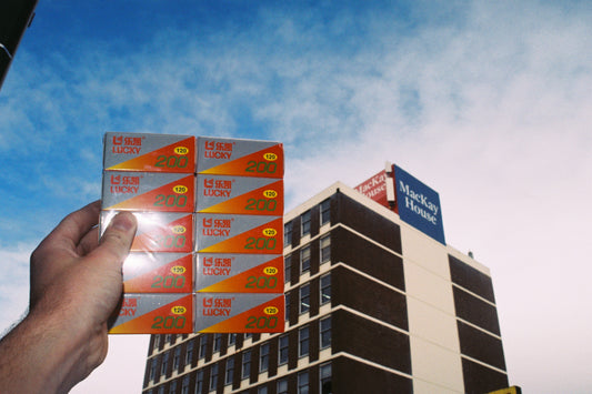 Sample shot: hand holding a block of Lucky 200 boxes against MacKay House and sky