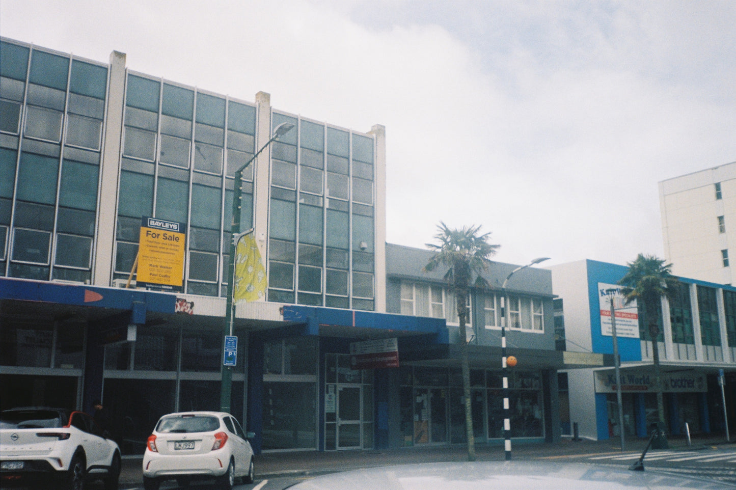 A film photograph of Commercial building with cars parked in front on a cloudy day