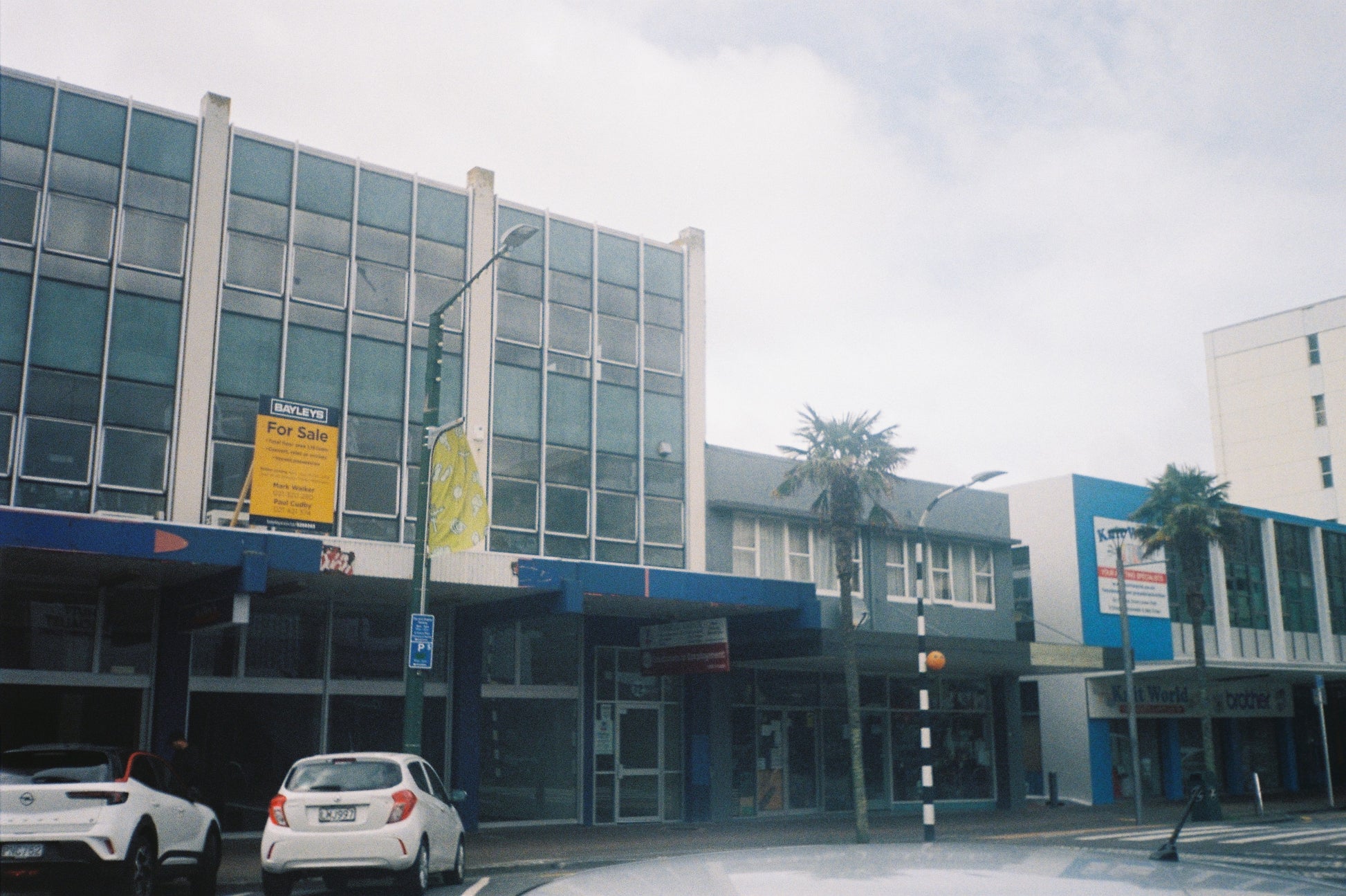 A film photograph of Commercial building with cars parked in front on a cloudy day