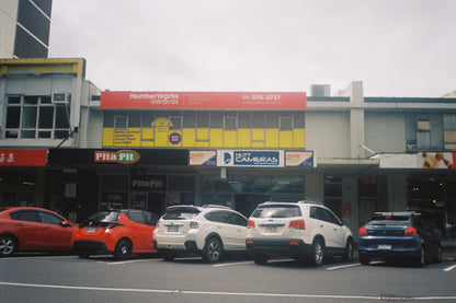 Film Photograph of Commercial building with various businesses including a Pita Pit restaurant and a camera store.