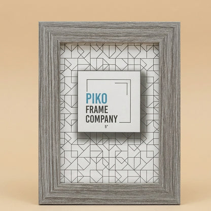 Grey woodgrain PIKO 5x7 photo frame standing on a beige background