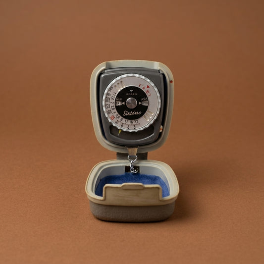 Sixtino light meter open in its cream case with blue lining, brown background