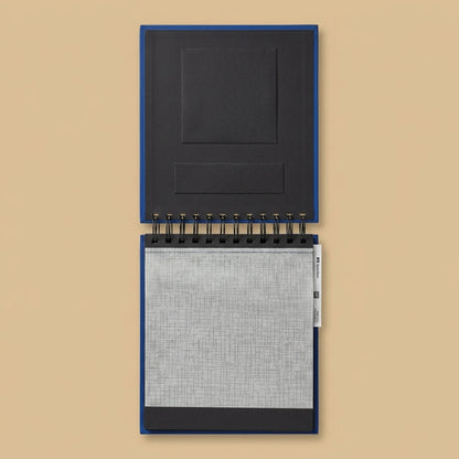 Hama spiral album opened flat, showing black pages and interleaving sheet, on a beige background