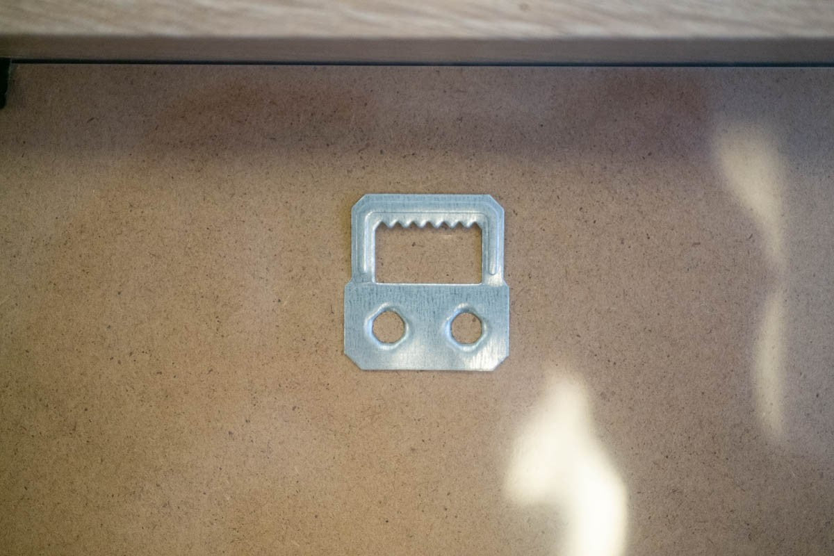 Close-up of metal sawtooth hanger fitted to the brown backing board of a 12x16 frame