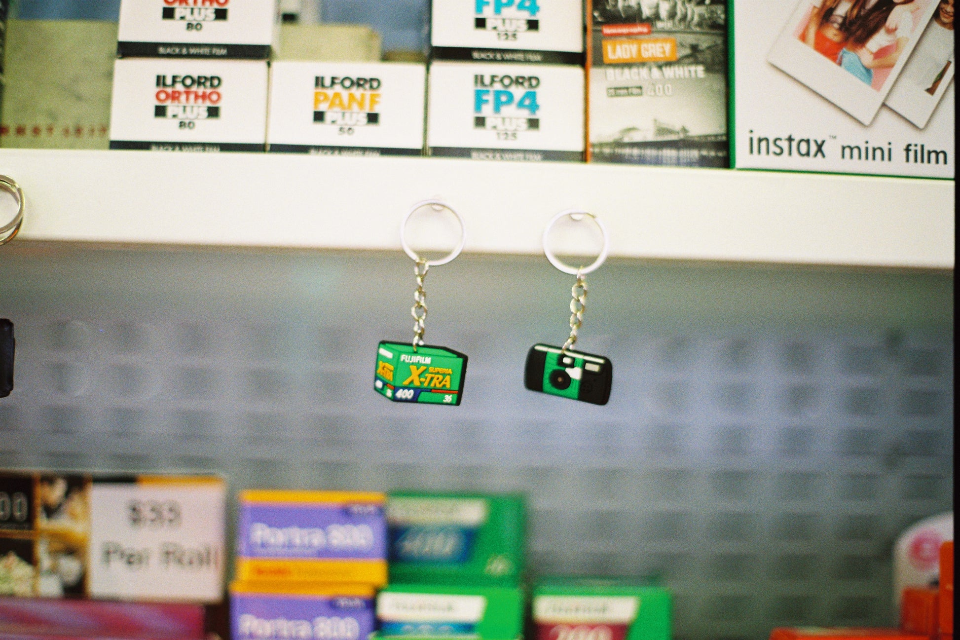 Two keychains resembling film packaging on a shelf with photography supplies in the background.