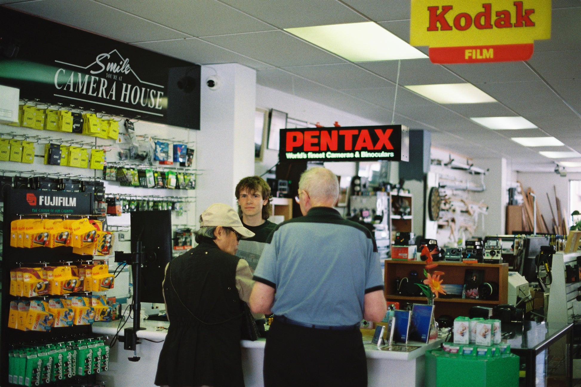 People shopping in a camera store with various camera equipment and brand signs.